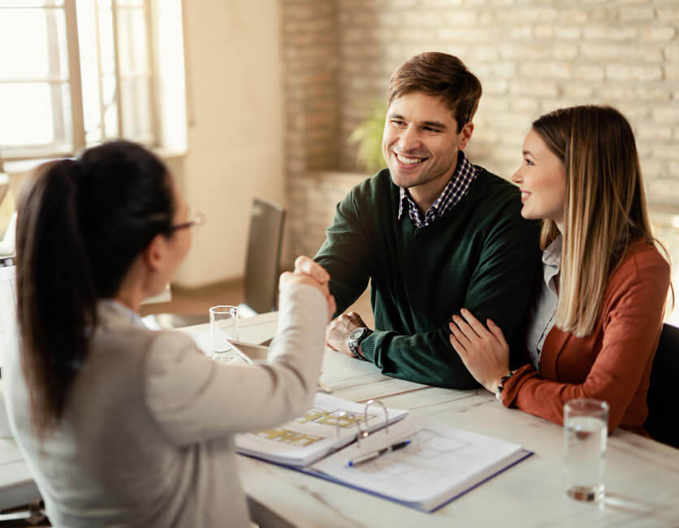Professional conveyancer at Eagle Peak shaking hands with happy clients across a desk, finalising property paperwork.